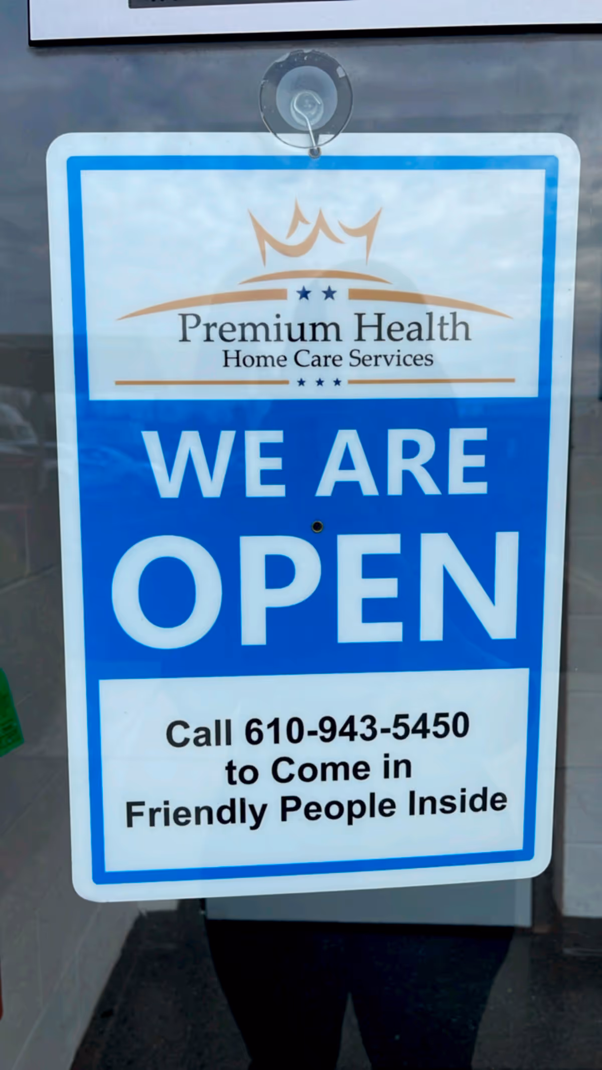 Blue 'WE ARE OPEN' sign for Premium Health Home Care Services on glass.