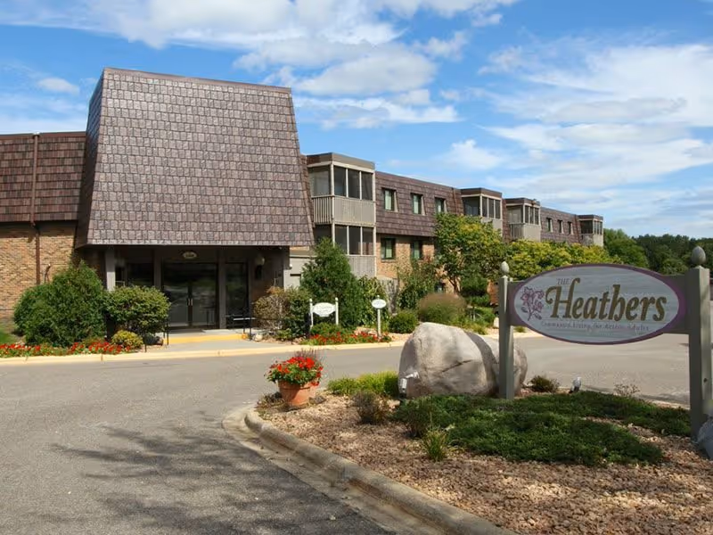 Exterior of Heathers Estates senior living building with entrance and landscaped surroundings.