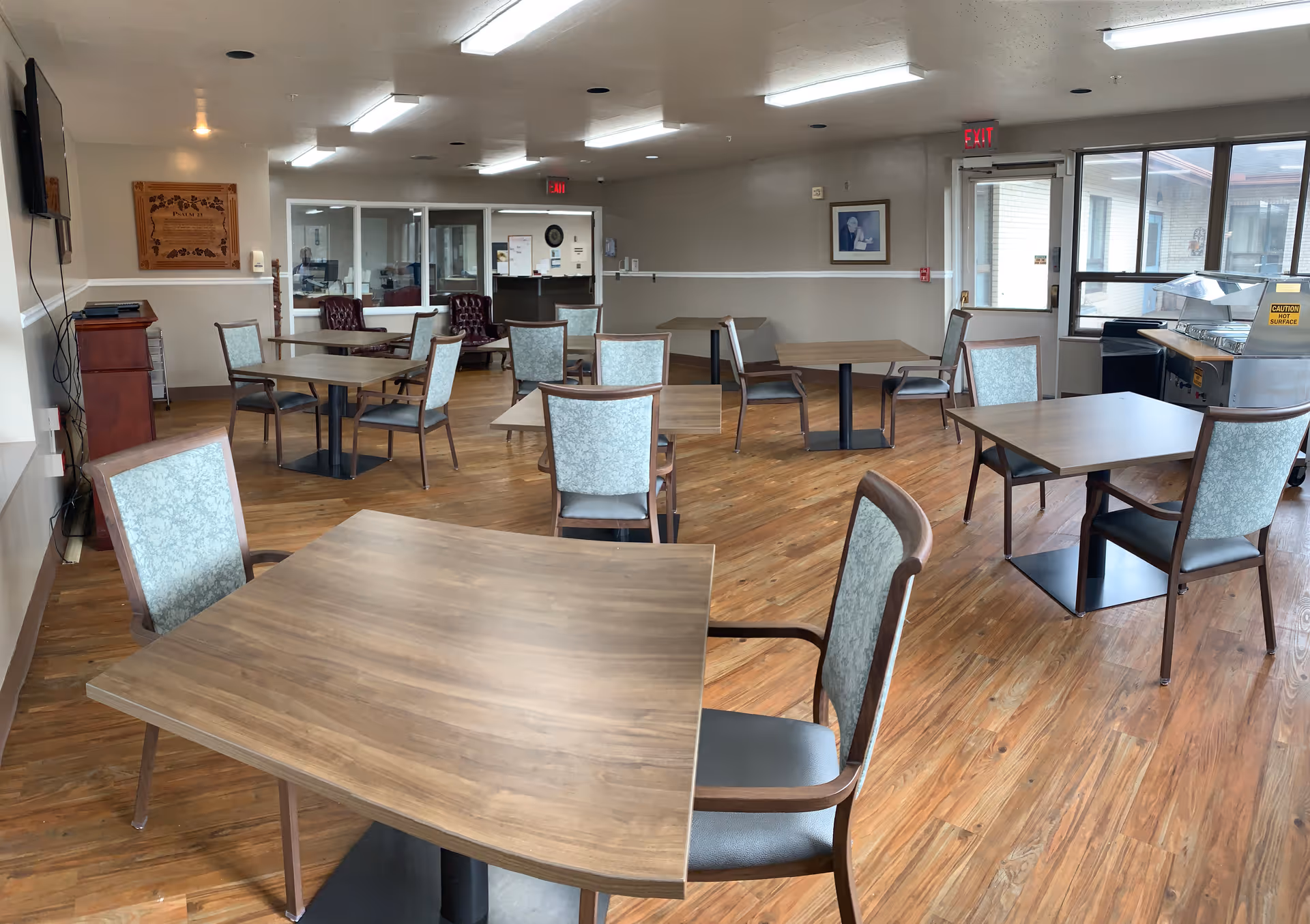 Spacious dining area with multiple tables and upholstered chairs in a senior facility.