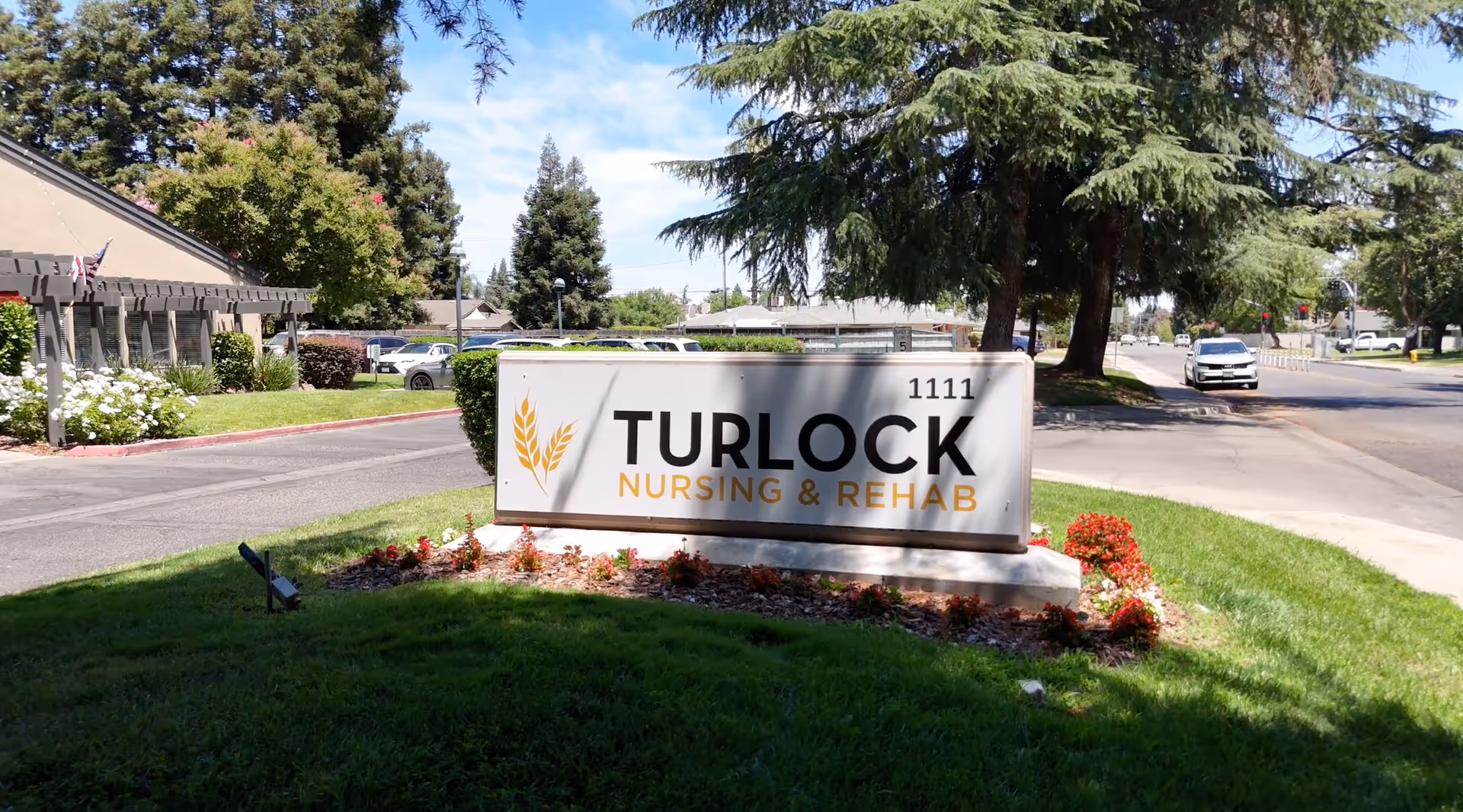 An exterior sign for Turlock Nursing & Rehab sits on a grassy island near the street.