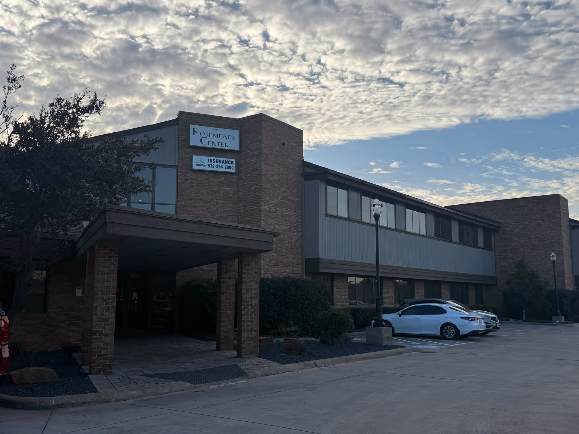 Exterior view of a brick senior living center with entrance canopy and parked cars.