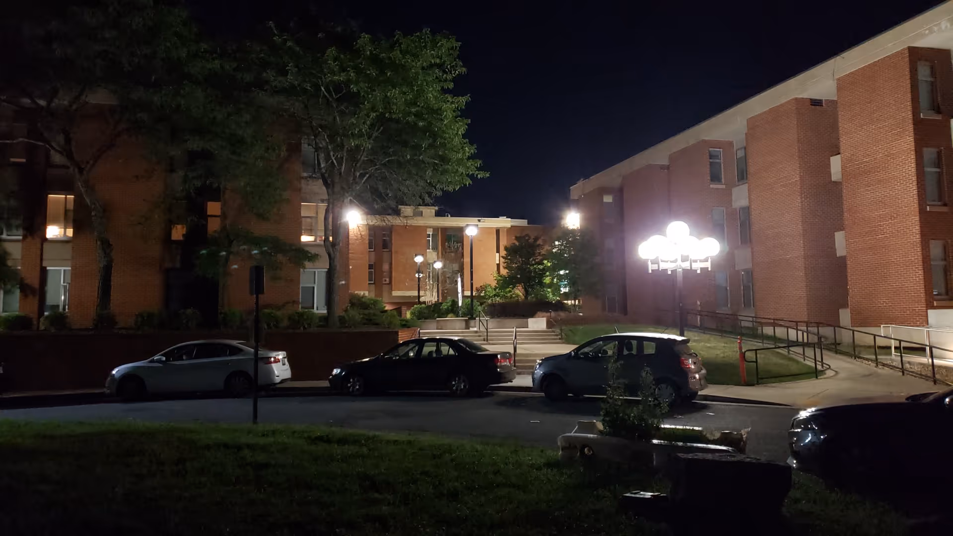 Night exterior of Abrams Hall Senior Apartments with parked cars and illuminated entrance.