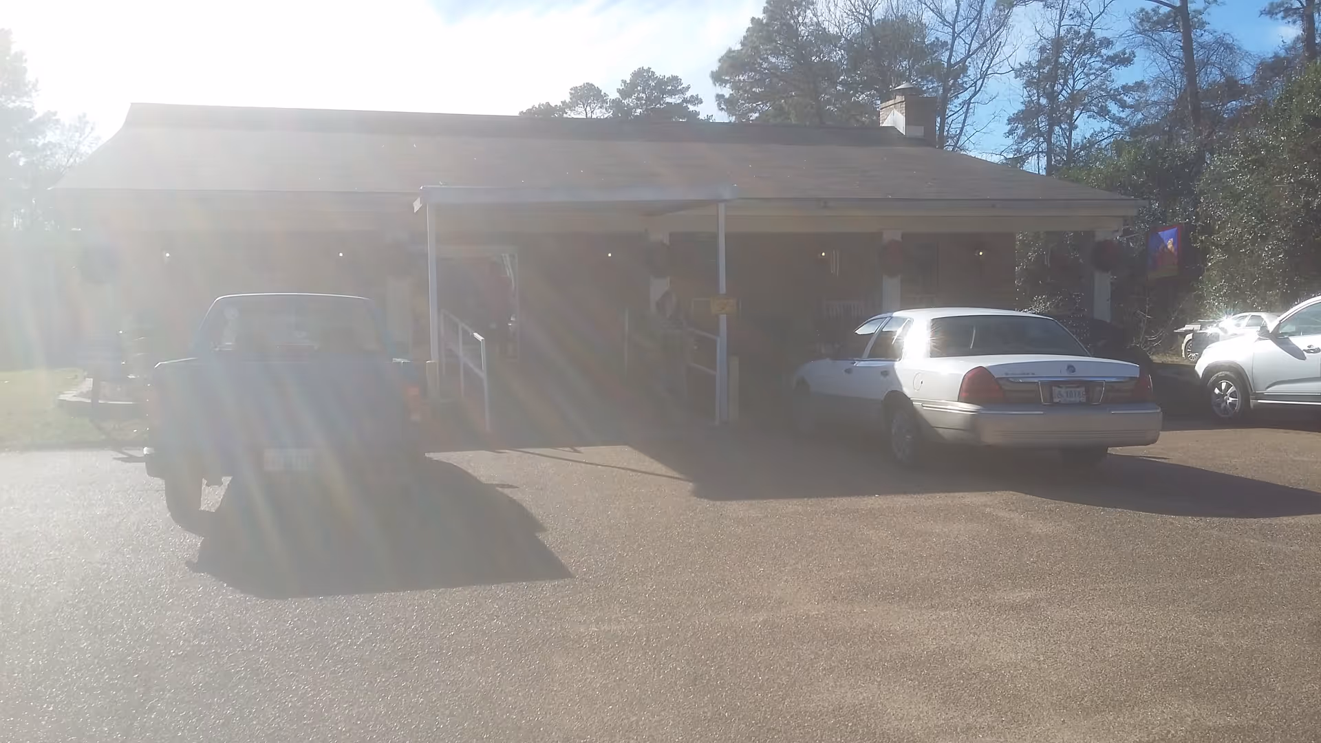 Sunlit facility entrance with parked cars under a covered drop-off area.
