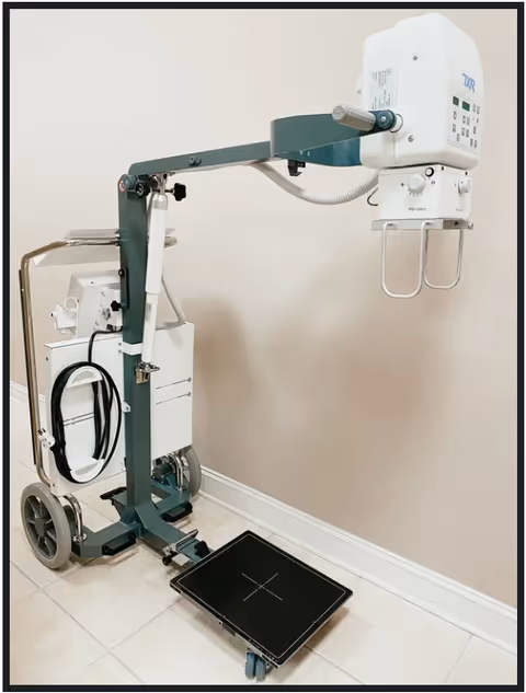Portable X-ray machine on a wheeled frame in a clinical room.