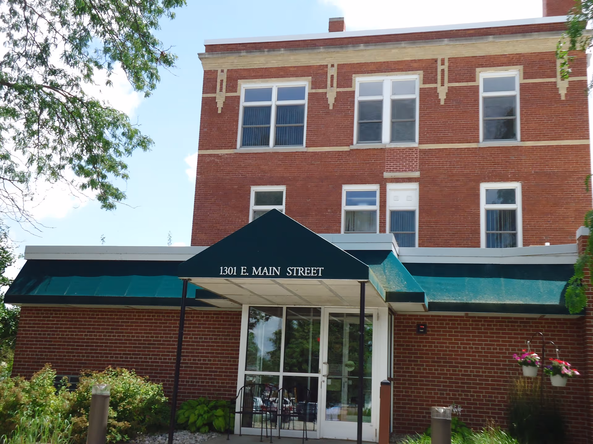 Brick three-story building front with a green awning reading "1301 E. MAIN STREET" over a glass entrance and landscaping.