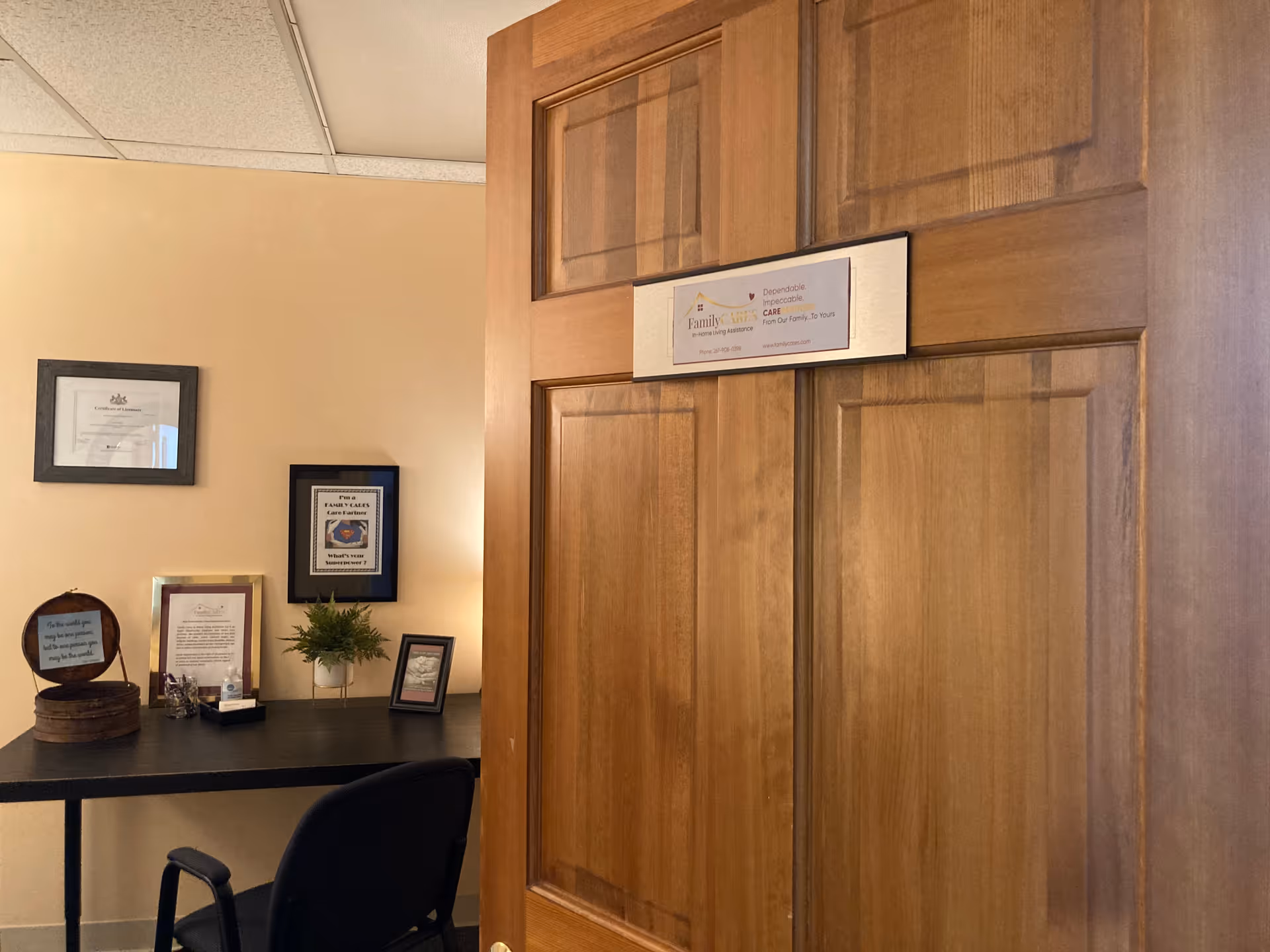 Wooden door partially open in a small office with certificates and a desk.