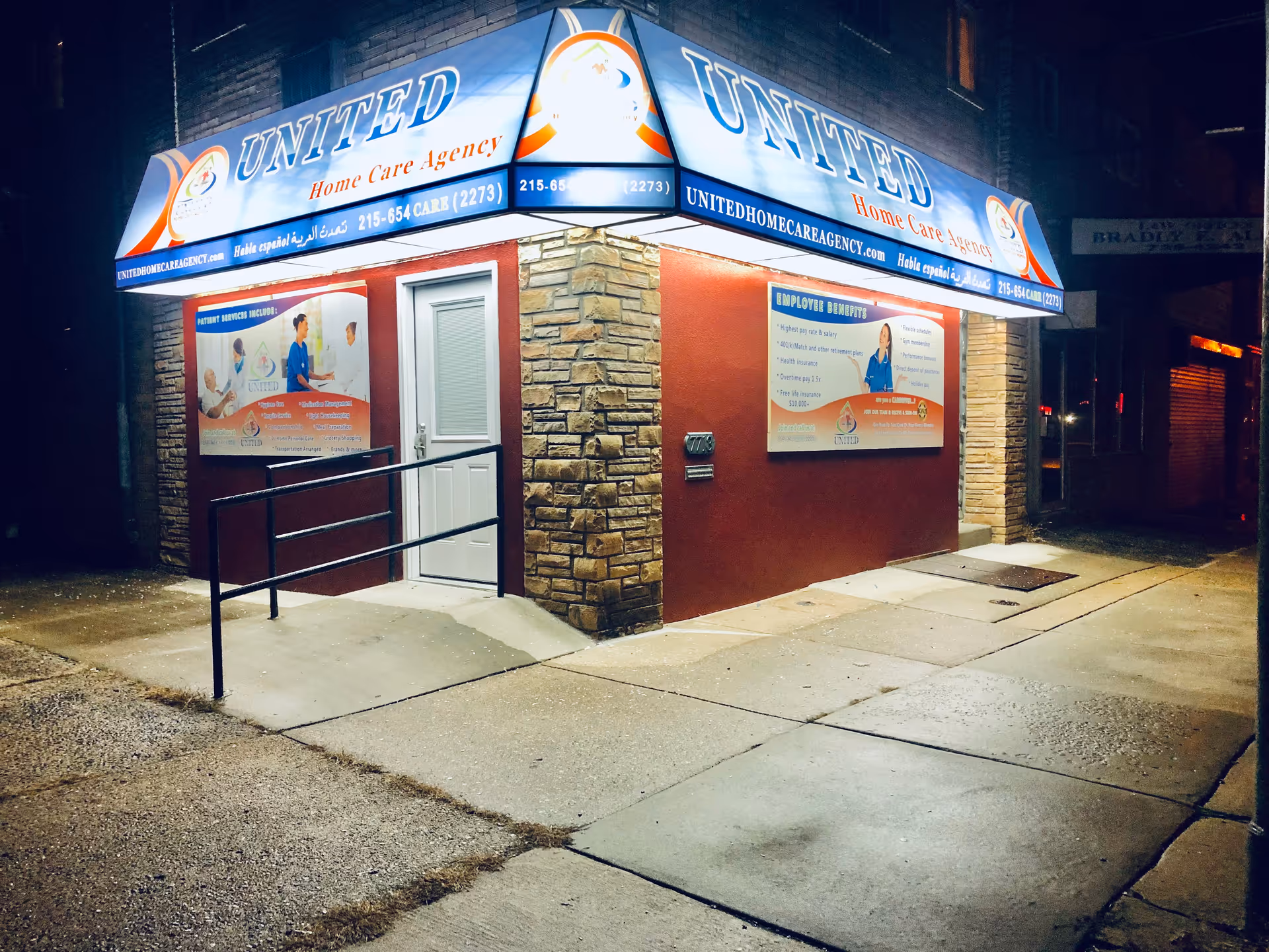 Night exterior of United Home Care Agency storefront with blue sign and stone facade.