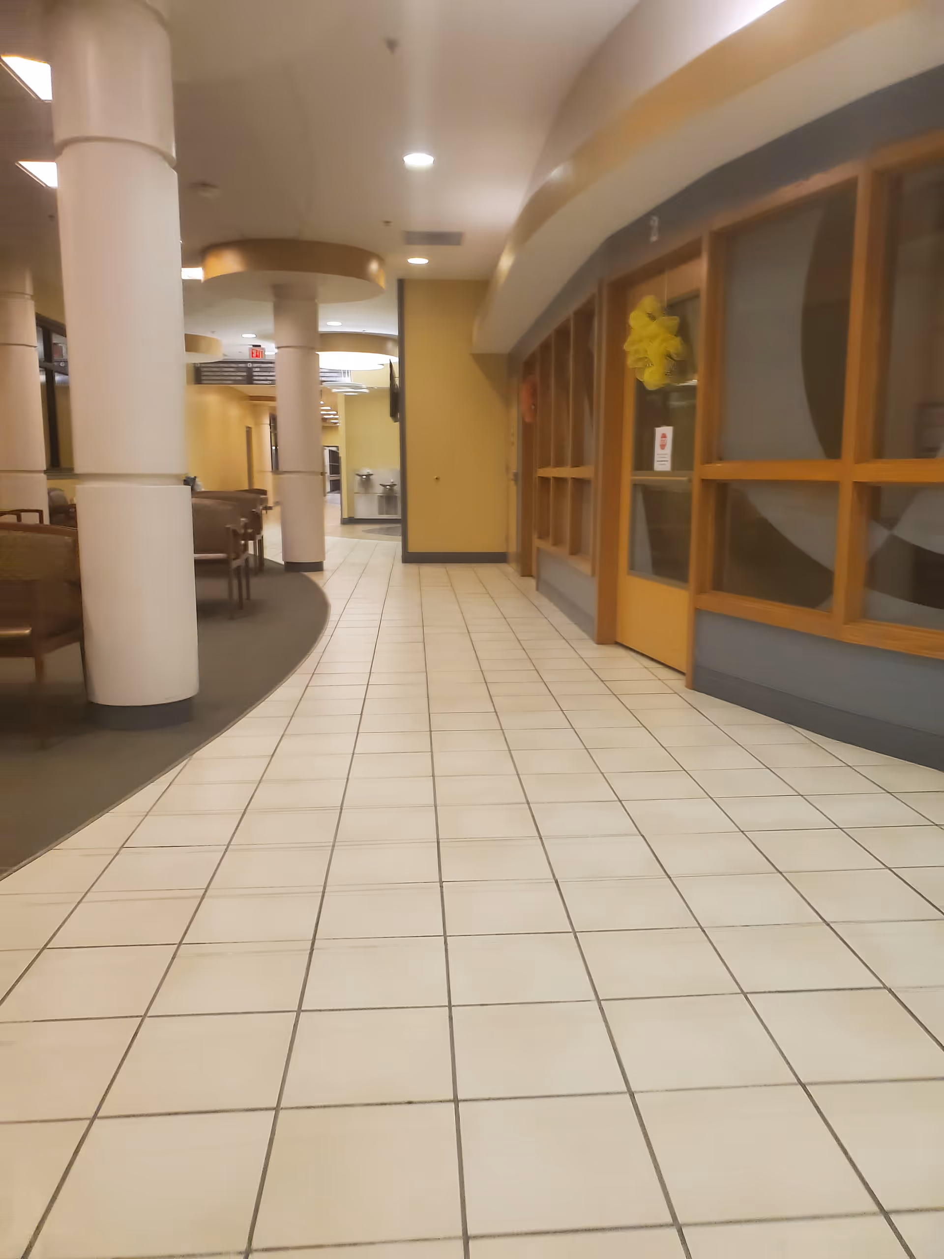 Wide interior hallway of West Calcasieu Cameron Hospital with tiled floor and glass-fronted rooms.