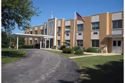 Front exterior of Misericordia Nursing and Rehabilitation Center, brick facade, entrance canopy, flagpole, manicured lawn.