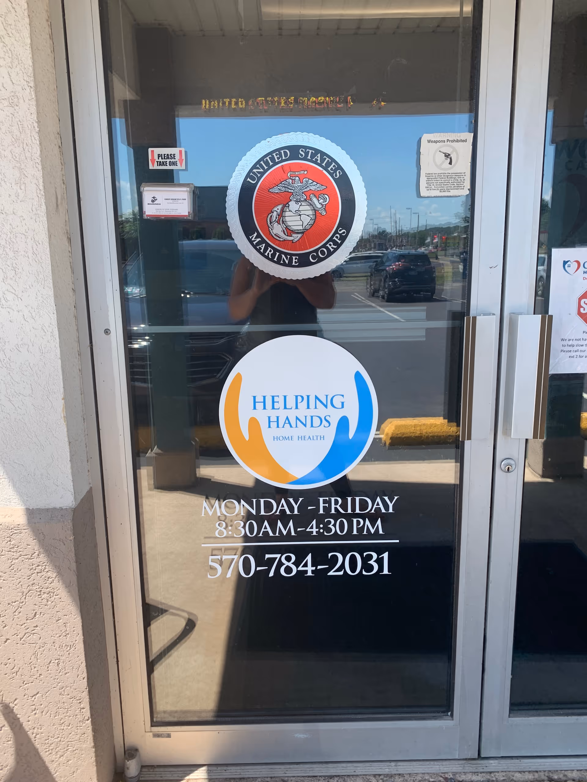 Glass entrance door with Marine Corps emblem, Helping Hands Home Health logos, hours and phone number.