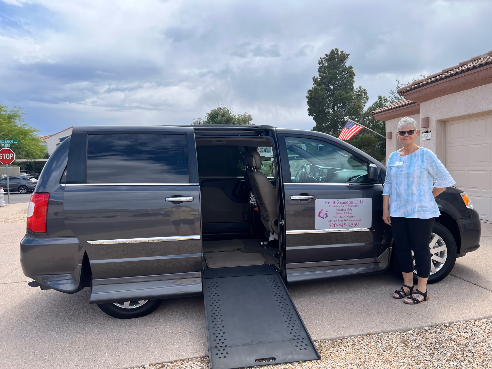 An adult woman stands beside a wheelchair-accessible van with a ramp outside a building.