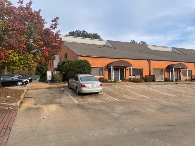 Exterior view of a brick nursing facility with a parking lot and trees.