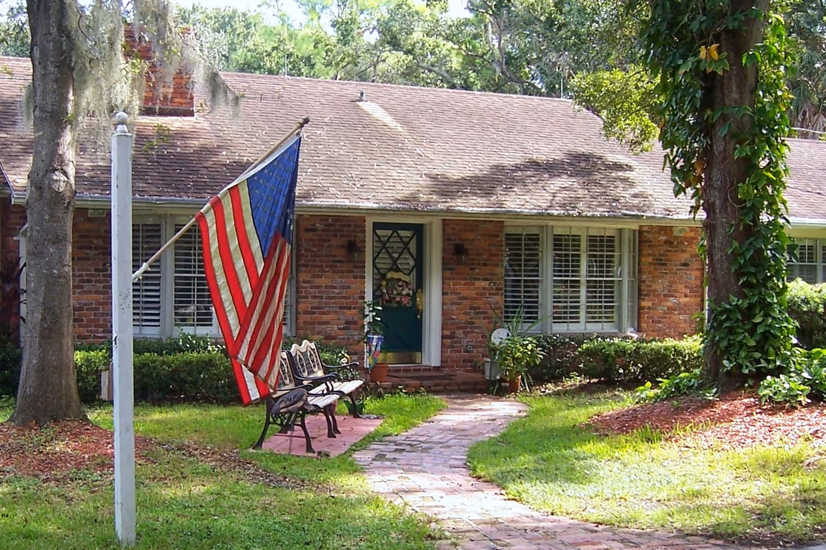 Front exterior of a brick-faced assisted living facility with flag, pathway, and benches.