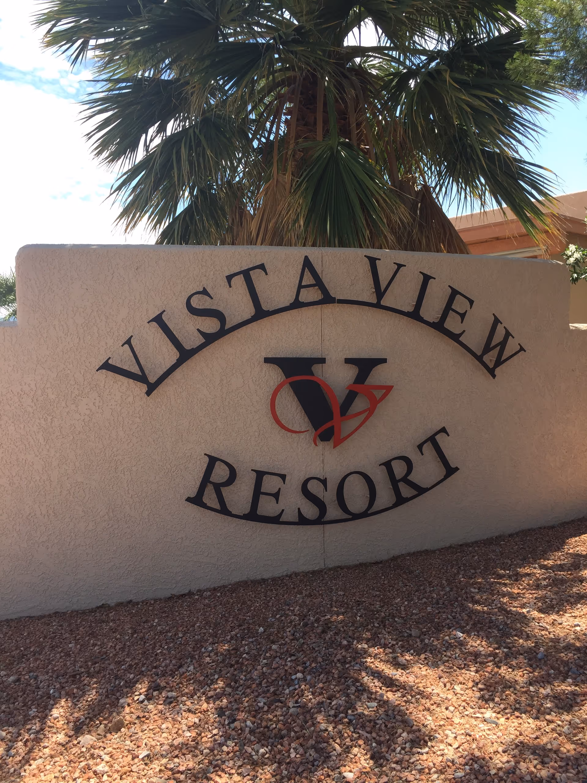 A stucco entrance sign reading 'Vista View Resort' with a palm tree behind and gravel in the foreground.