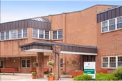 Brick senior living center entrance with glass doors and planters.