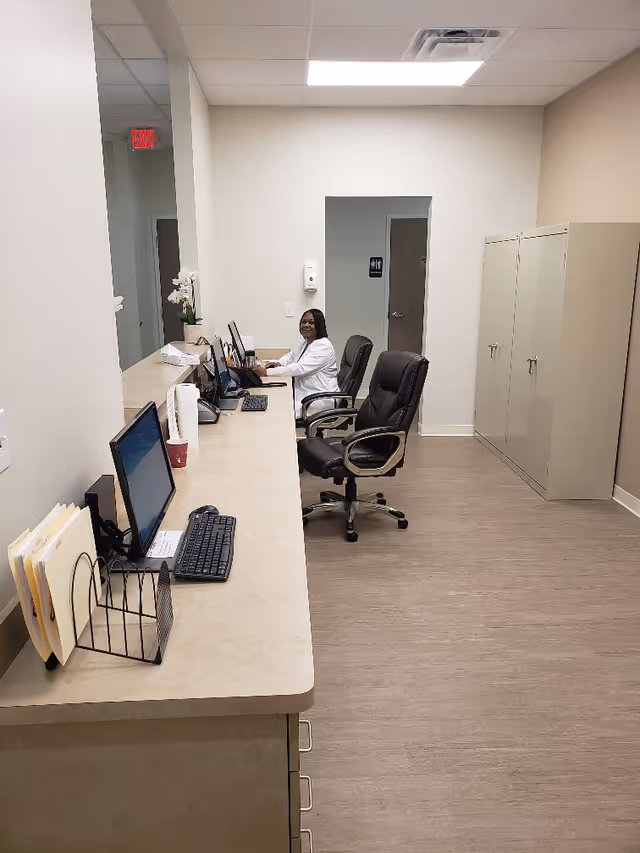 Clinic reception area with a long counter, computers, and a staff member seated.