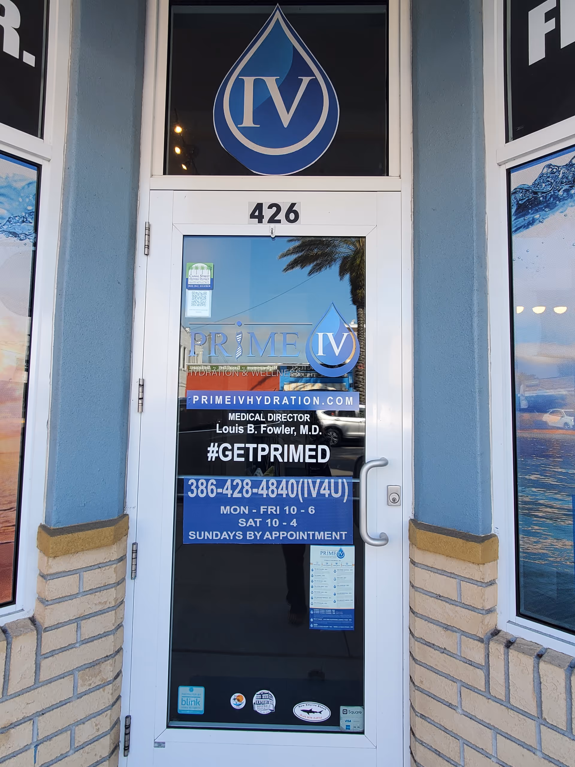 Front glass door with Prime IV Hydration logo and building signage, reflected street scene.