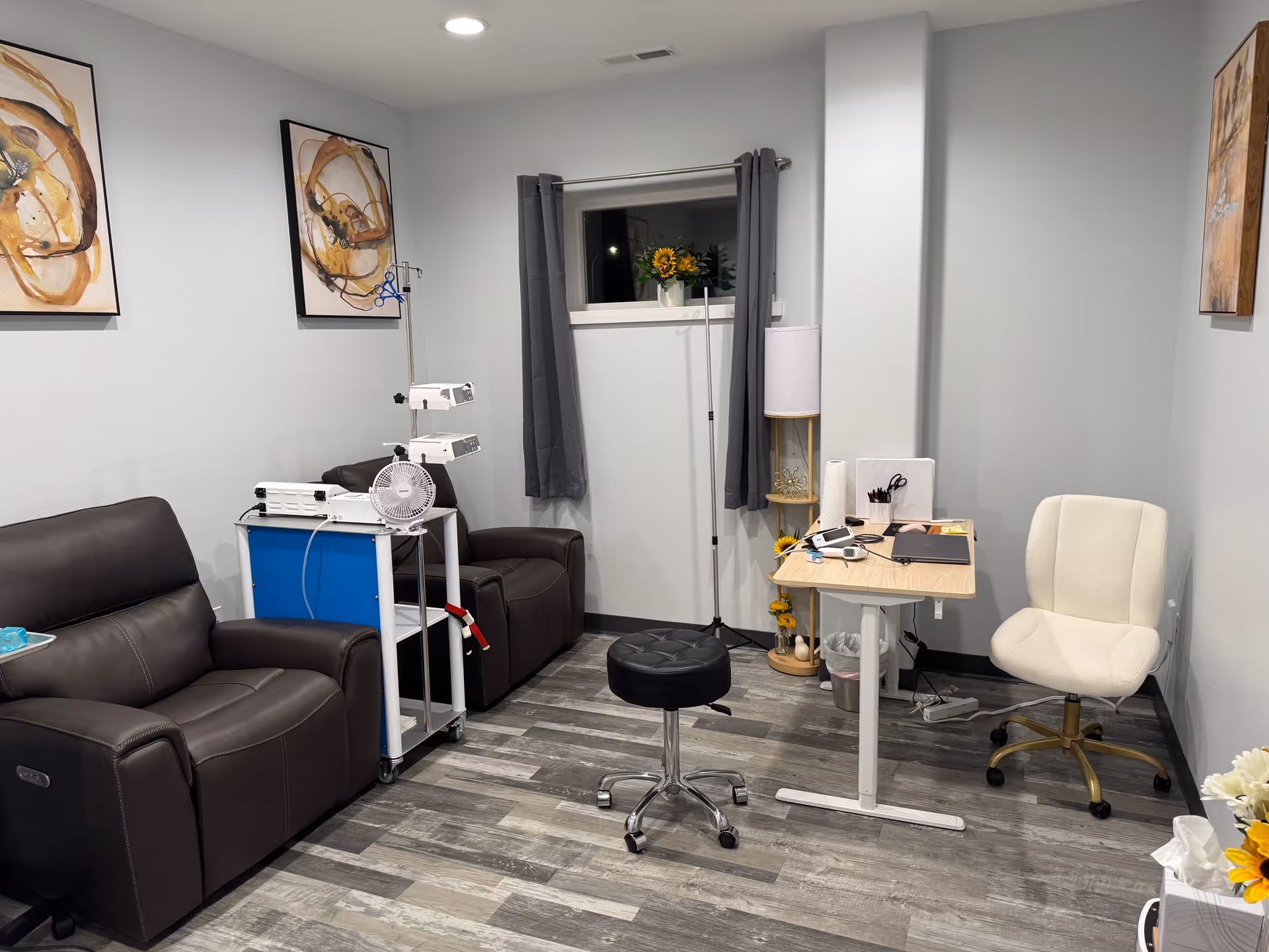 A small clinic-like room with leather sofas, a desk, and medical equipment by a window.