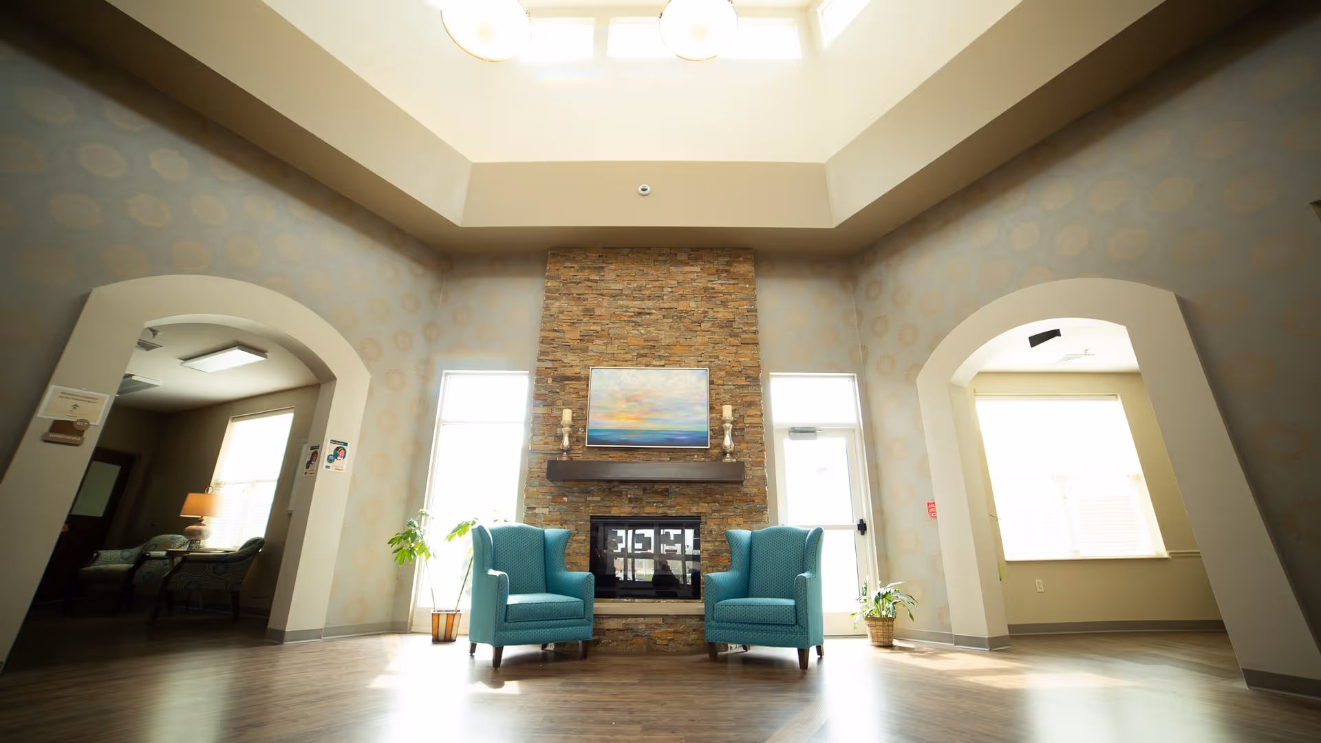 Spacious lobby living room with a brick fireplace, two teal armchairs, and arched doorways.