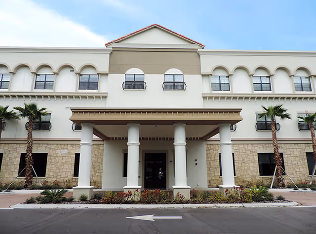 Front view of a beige senior living facility with tall white columns and palm trees.