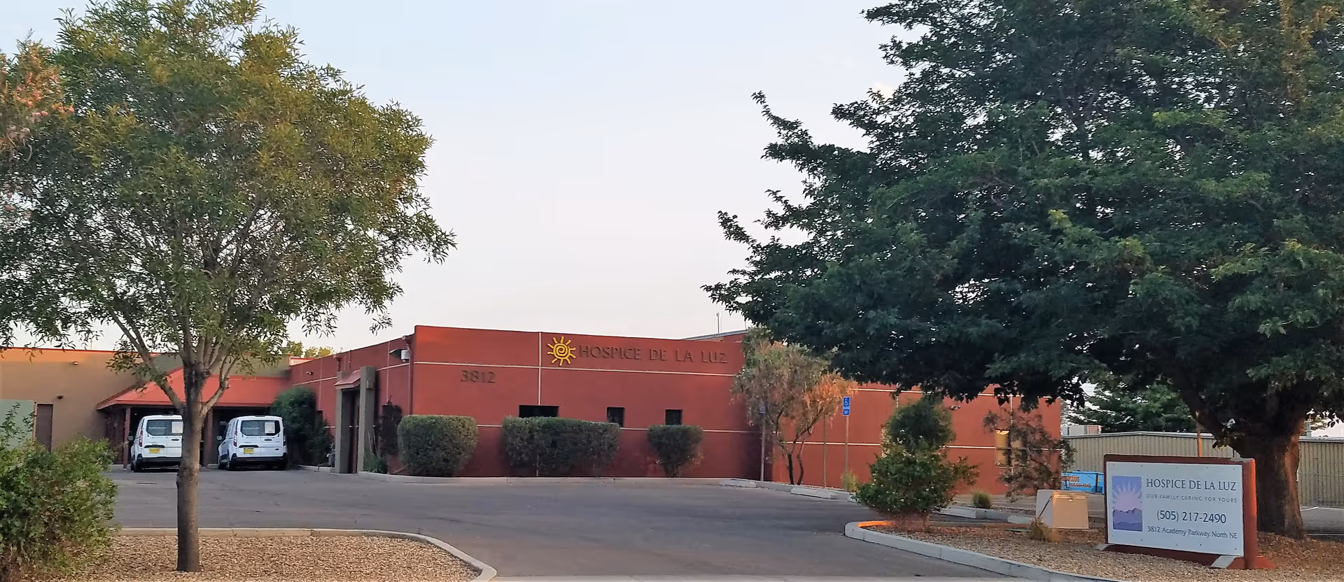 Exterior view of Hospice De La Luz building with trees and a parking lot.