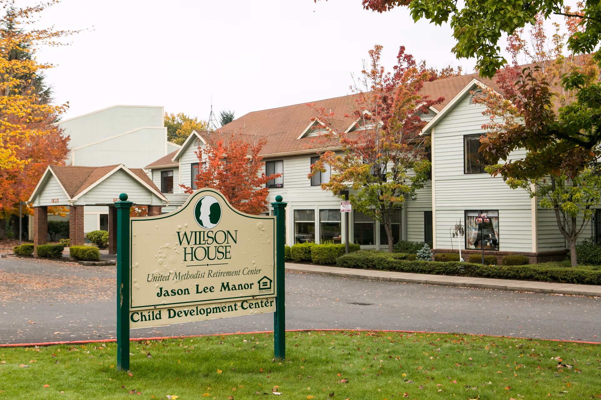Exterior view of Willson House Residential Care with sign and autumn trees.