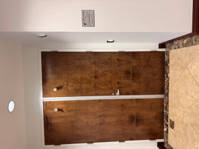 Double wooden doors in a hallway with a tiled floor and granite countertop on the right.