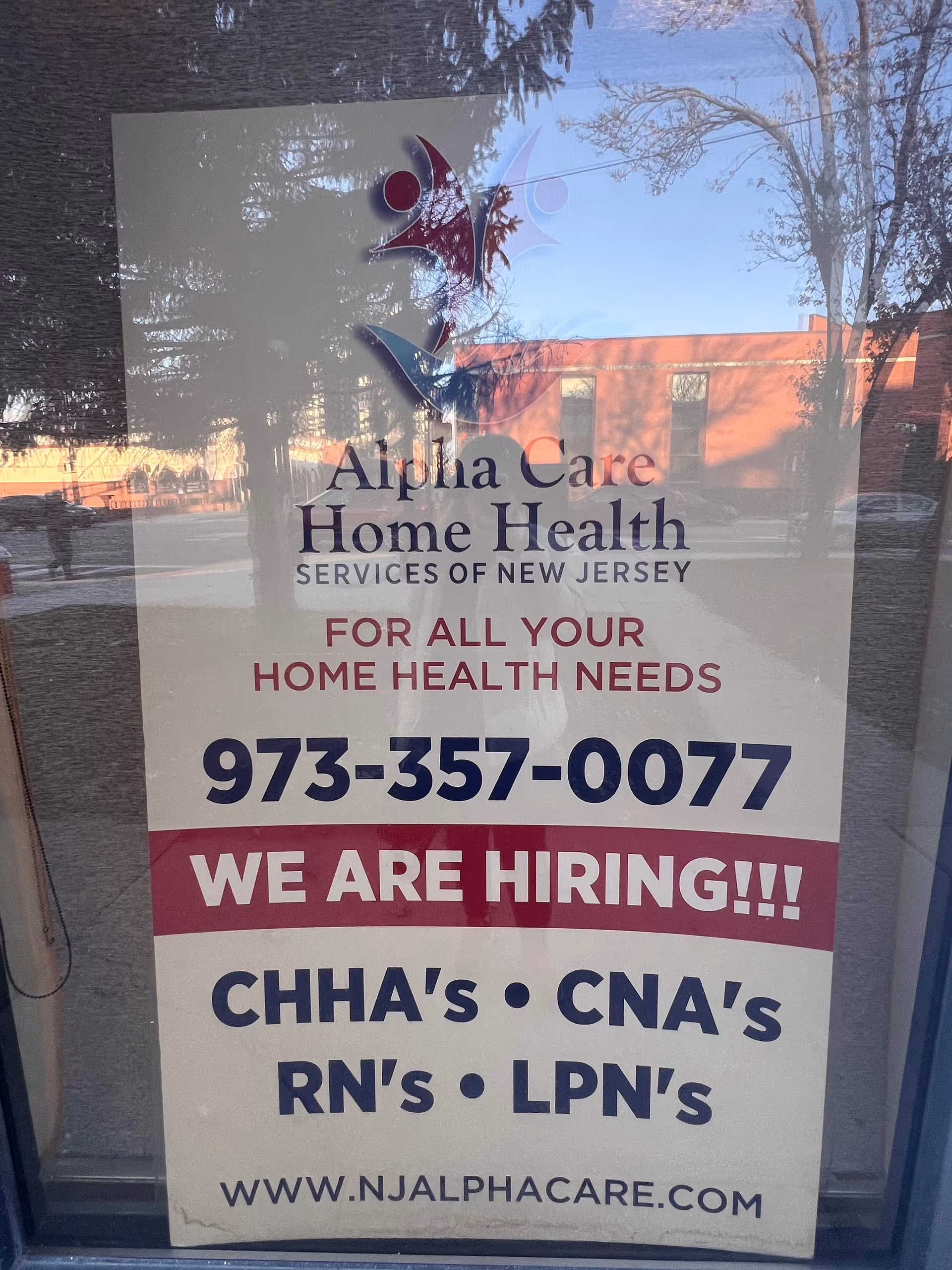 Storefront window sign advertising Alpha Care Home Health and hiring, with phone 973-357-0077.