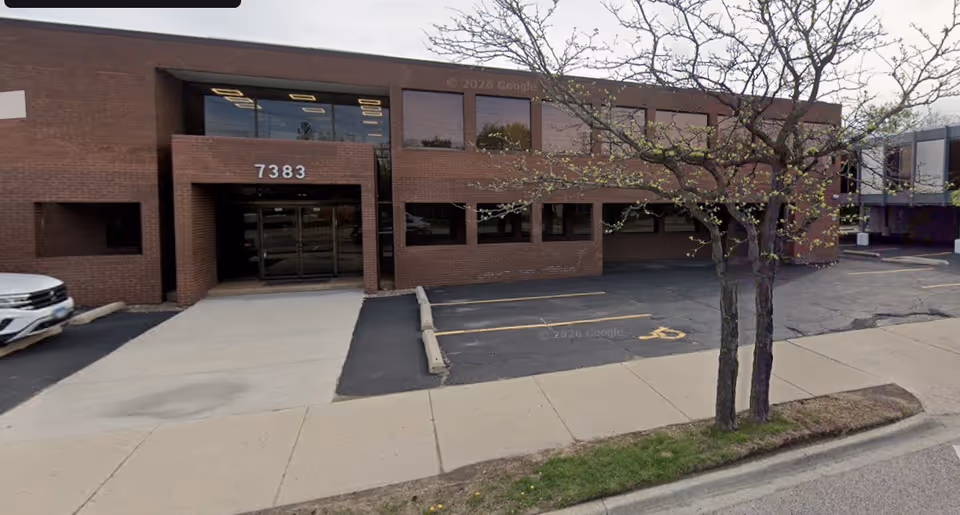 Brick building exterior with glass entrance and tree-lined sidewalk.