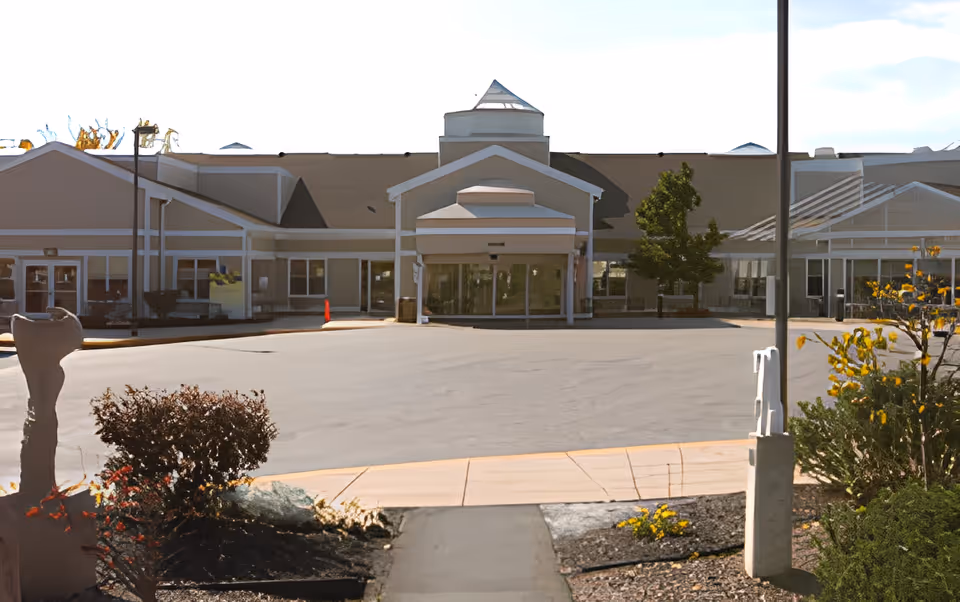 Front exterior view of Dosberg Manor Adlt Hme-Menorah building with a paved driveway, landscaped bushes, and a sidewalk leading to the entrance under a covered portico.