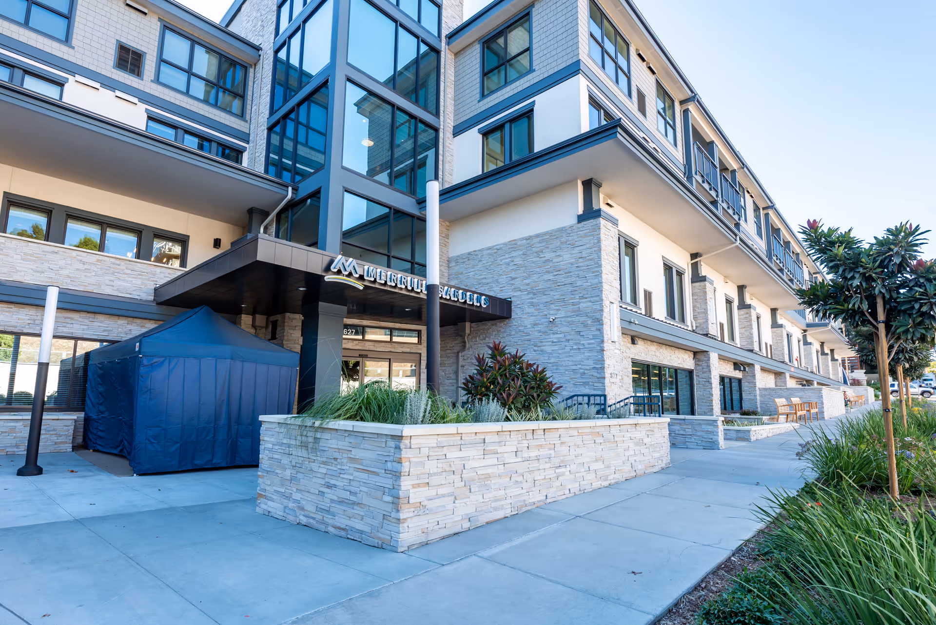 Modern multi-story senior living building with a glass facade, covered entrance, and sidewalk.