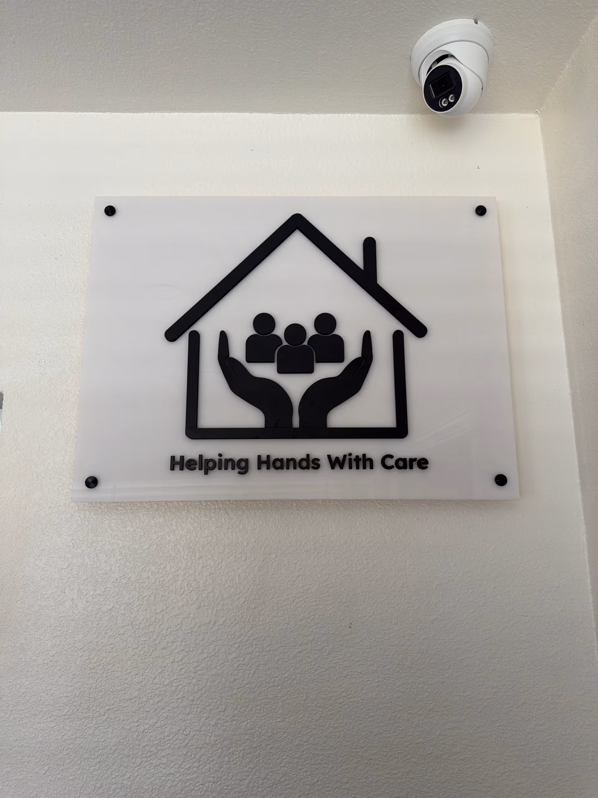 Exterior wall sign for Helping Hands With Care featuring a house and hands logo.