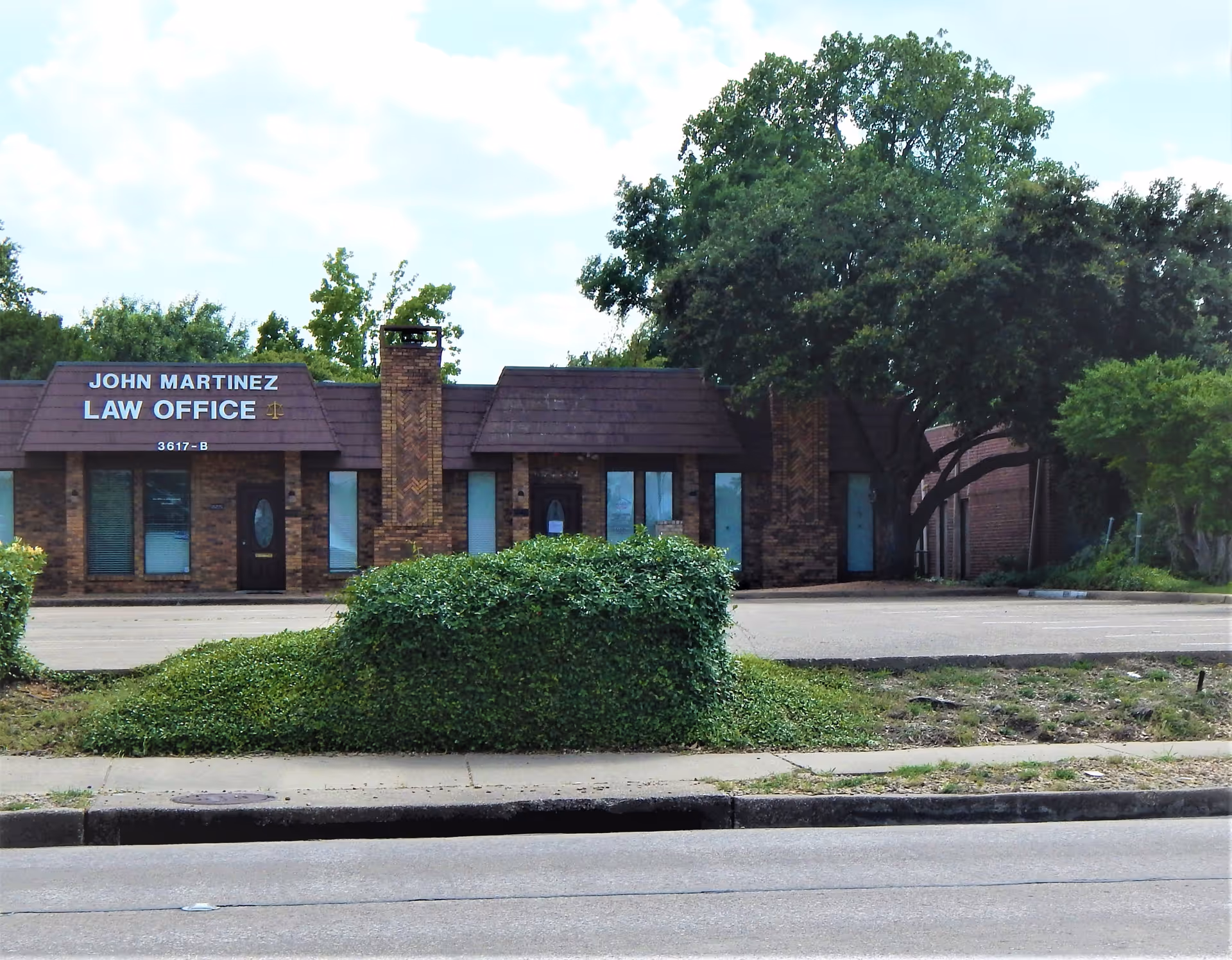 Brick office building with a sign, glass doors, and a manicured hedge in front.