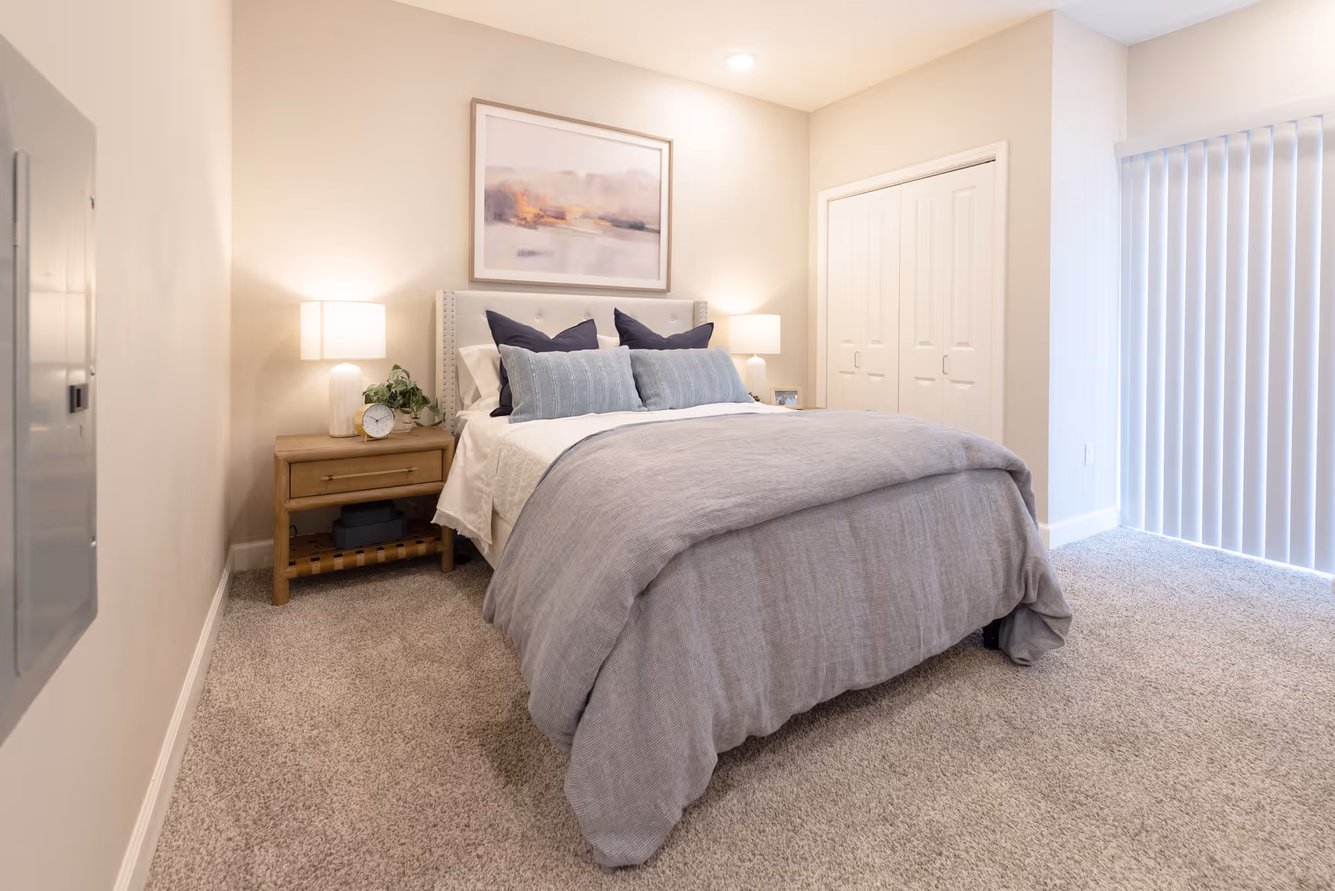 A cozy bedroom with a neatly made bed, bedside lamps, and vertical blinds.