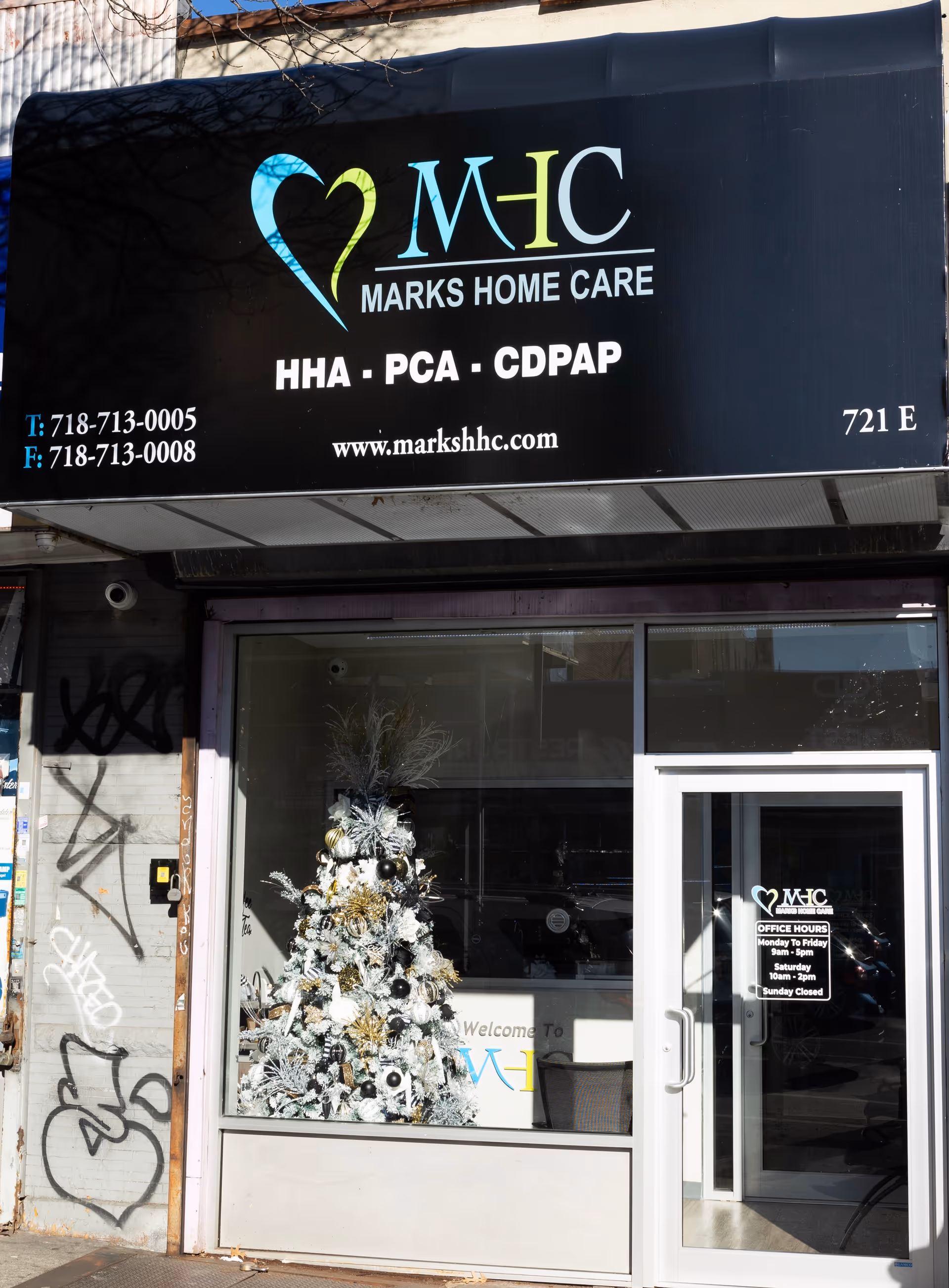 Black storefront sign reads Marks Home Care with heart logo above glass entrance, Christmas tree inside.