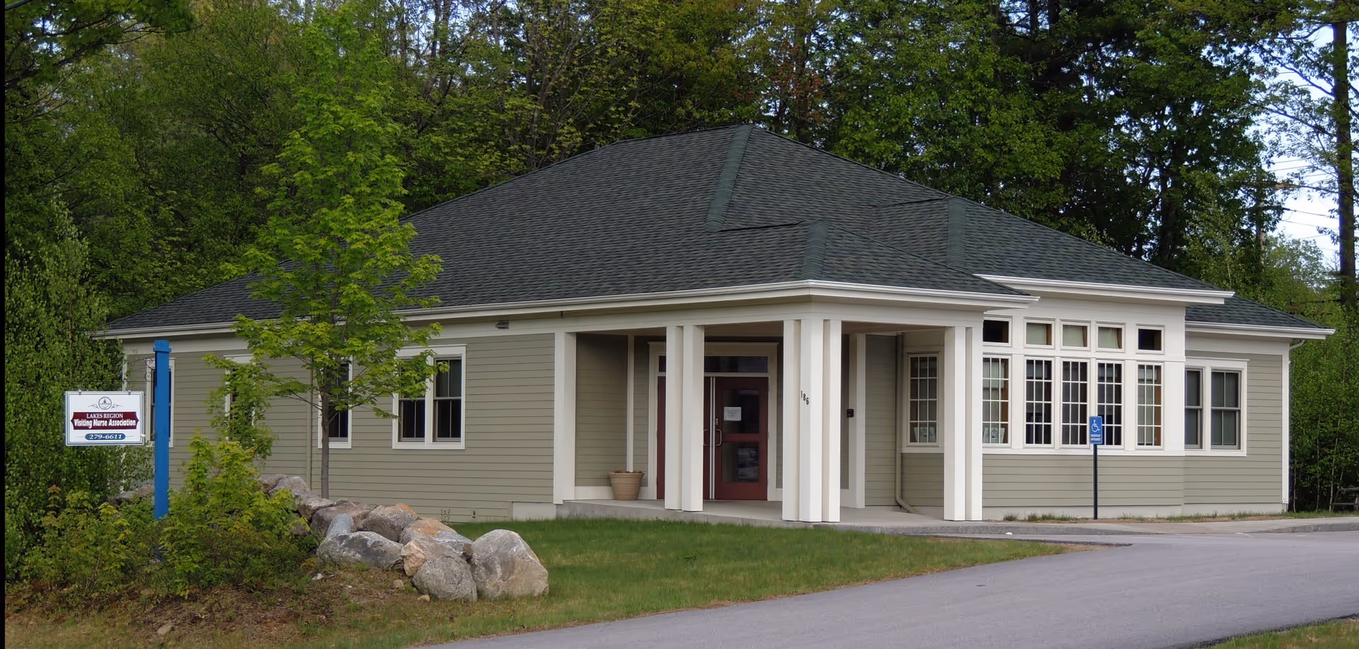 A single-story beige building with a covered entrance and surrounding green landscape.