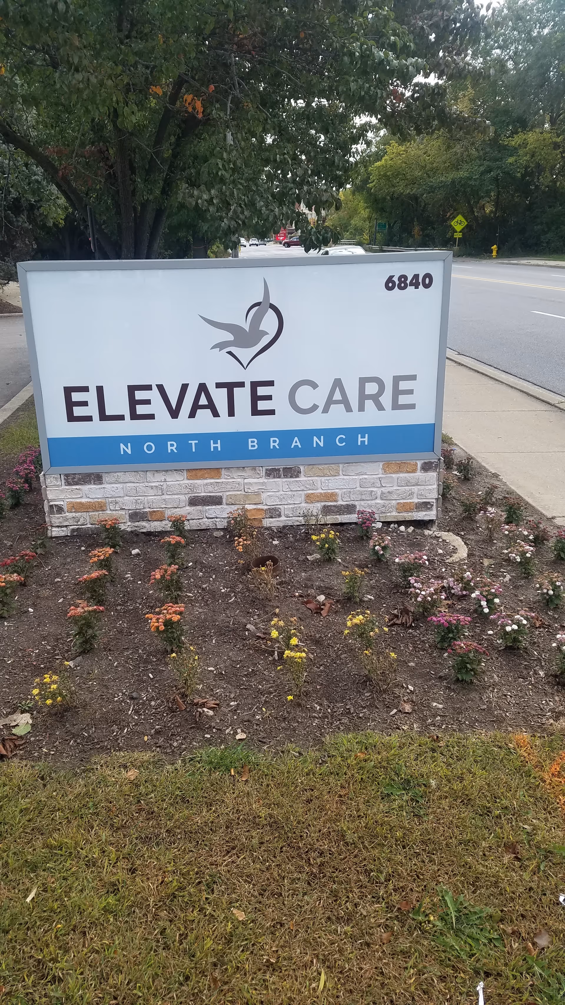 Large sign reading Elevate Care North Branch beside a planted flower bed.
