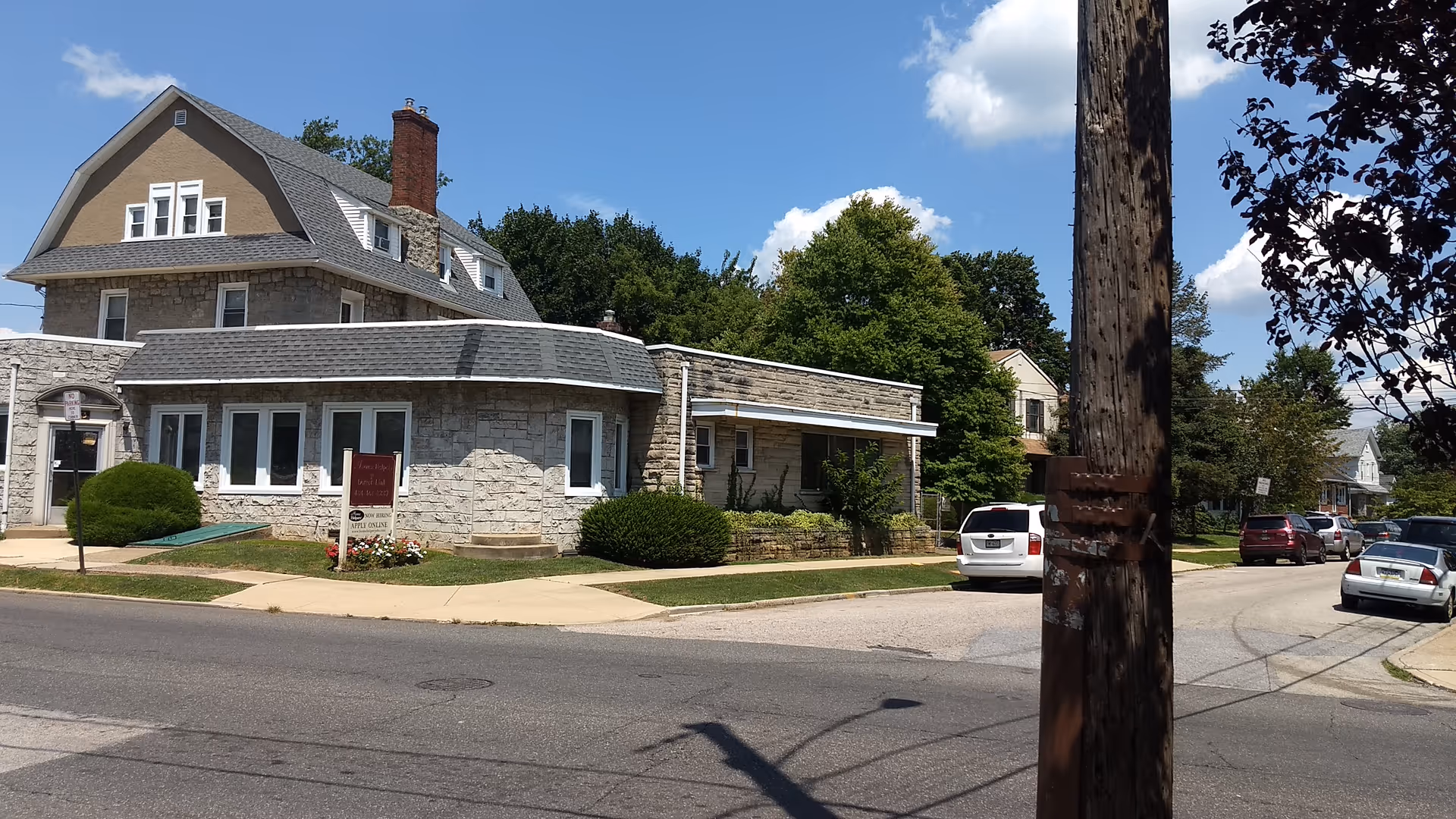 Stone-faced senior living facility on a tree-lined street with parked cars.