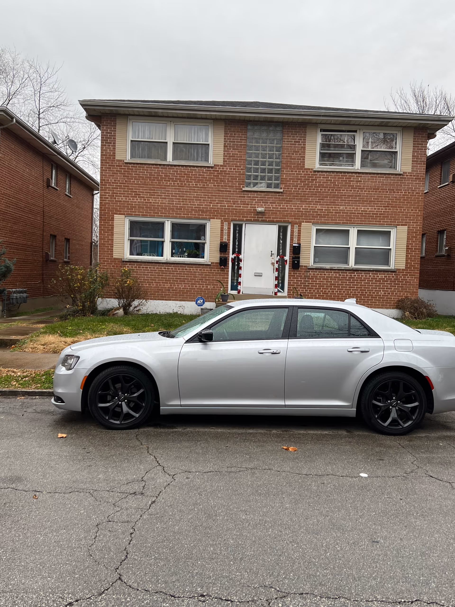 Two-story brick building with a white entrance door and a silver car in front.