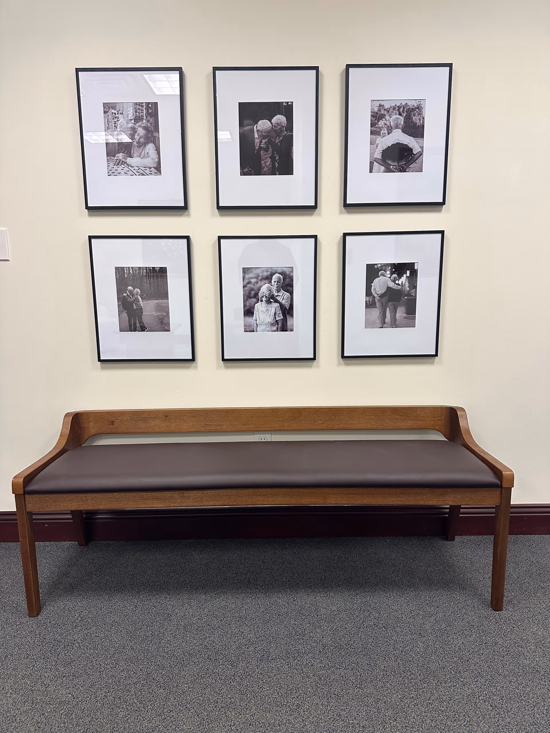 Wood bench with a padded seat sits against a wall decorated with six framed photos.