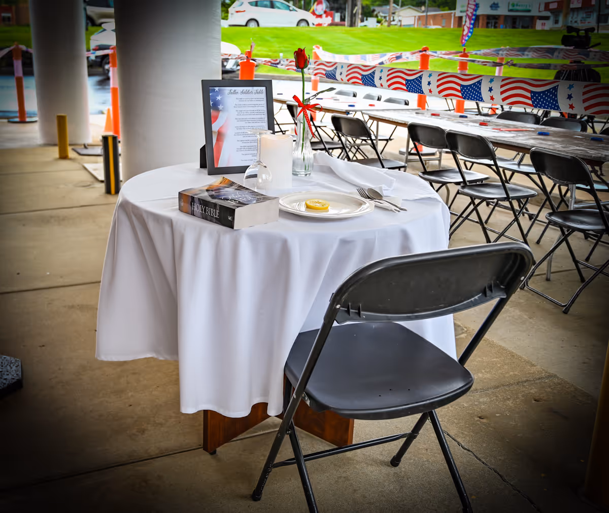 Outdoor event setup with a round table, white cloth, Bible, and patriotic decorations.