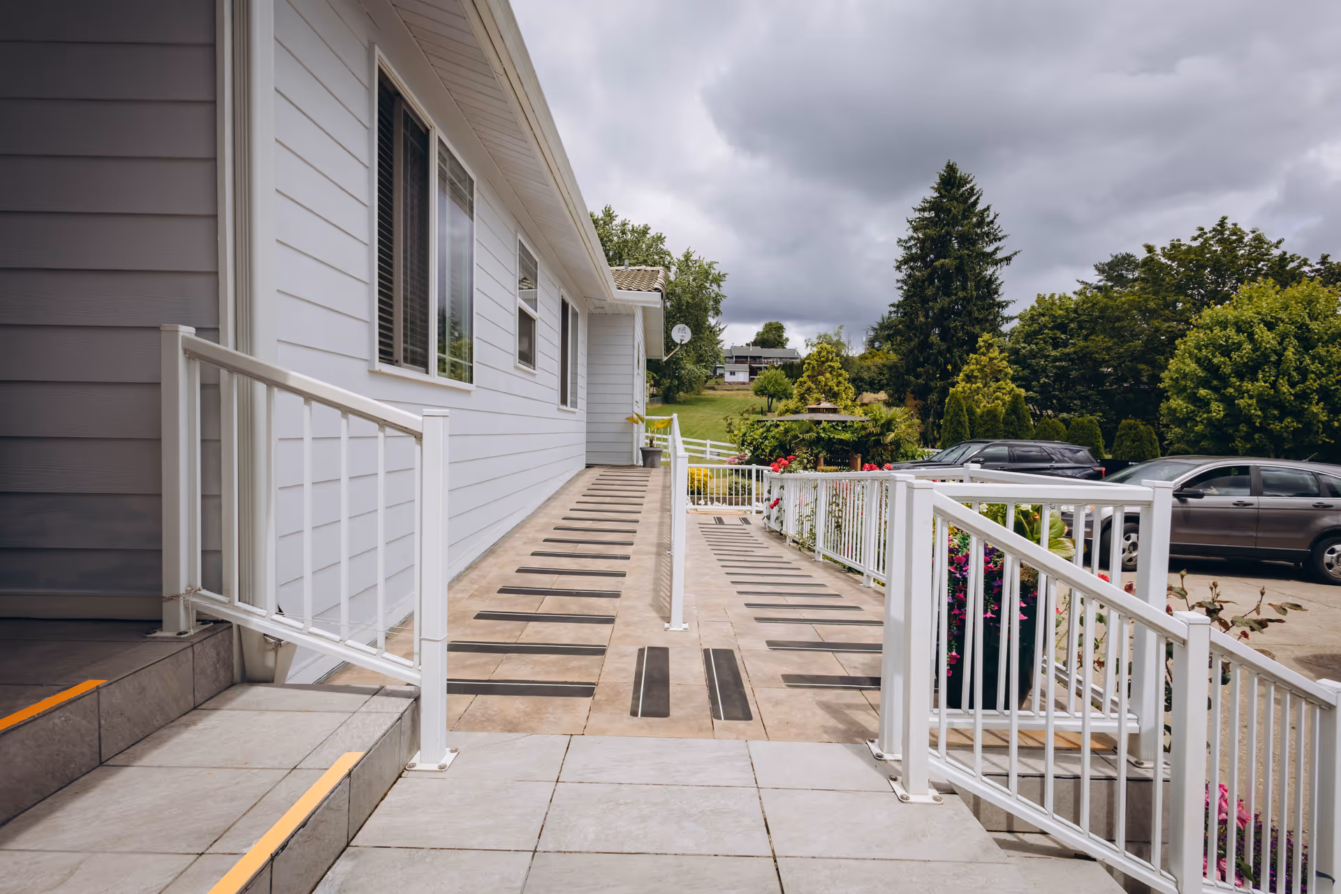 Exterior walkway and ramp beside a light gray senior living facility, with parked cars nearby.