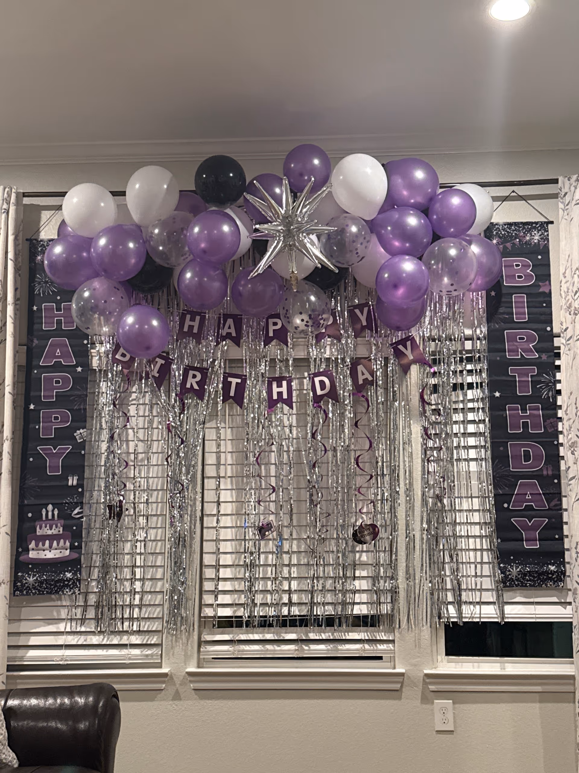Purple, white, and black birthday decorations with balloons and silver tinsel hang in a room.