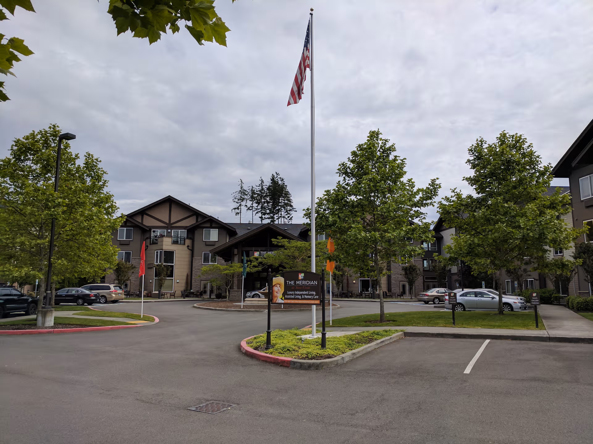 Exterior view of Meridian at Stone Creek, with flagpole, trees, and parked cars.