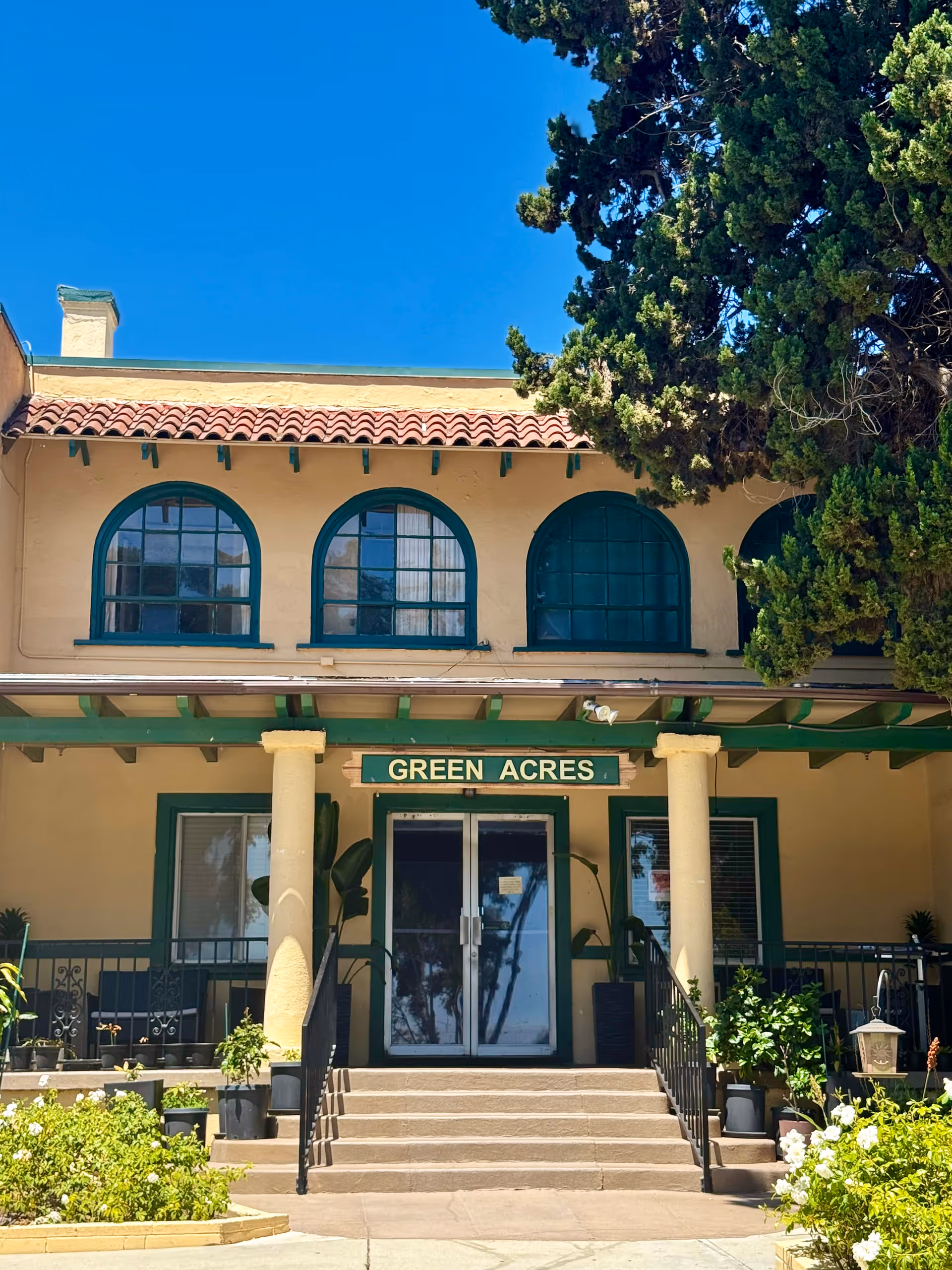 Green Acres Lodge front entrance with arched blue windows, columns, and lush greenery.