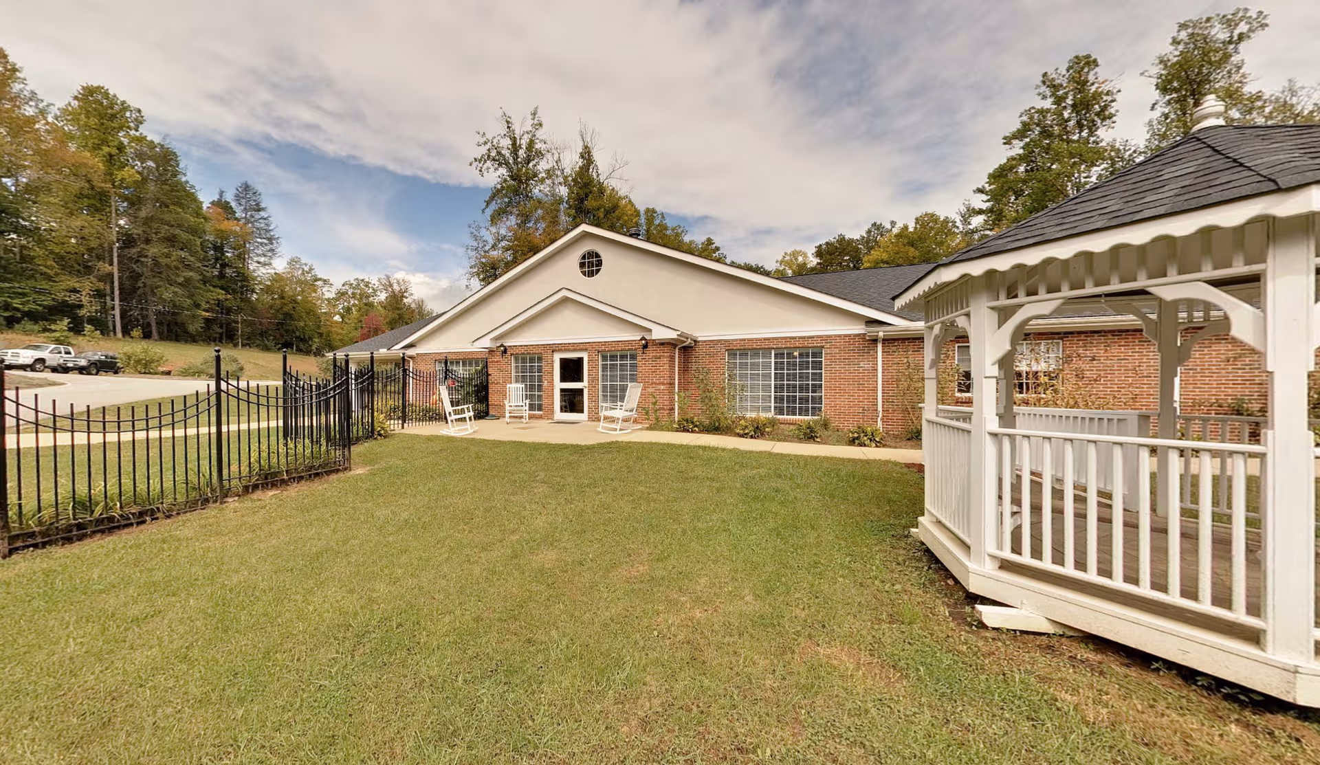 Brick facility with a manicured lawn, fence, chairs, and a white gazebo.