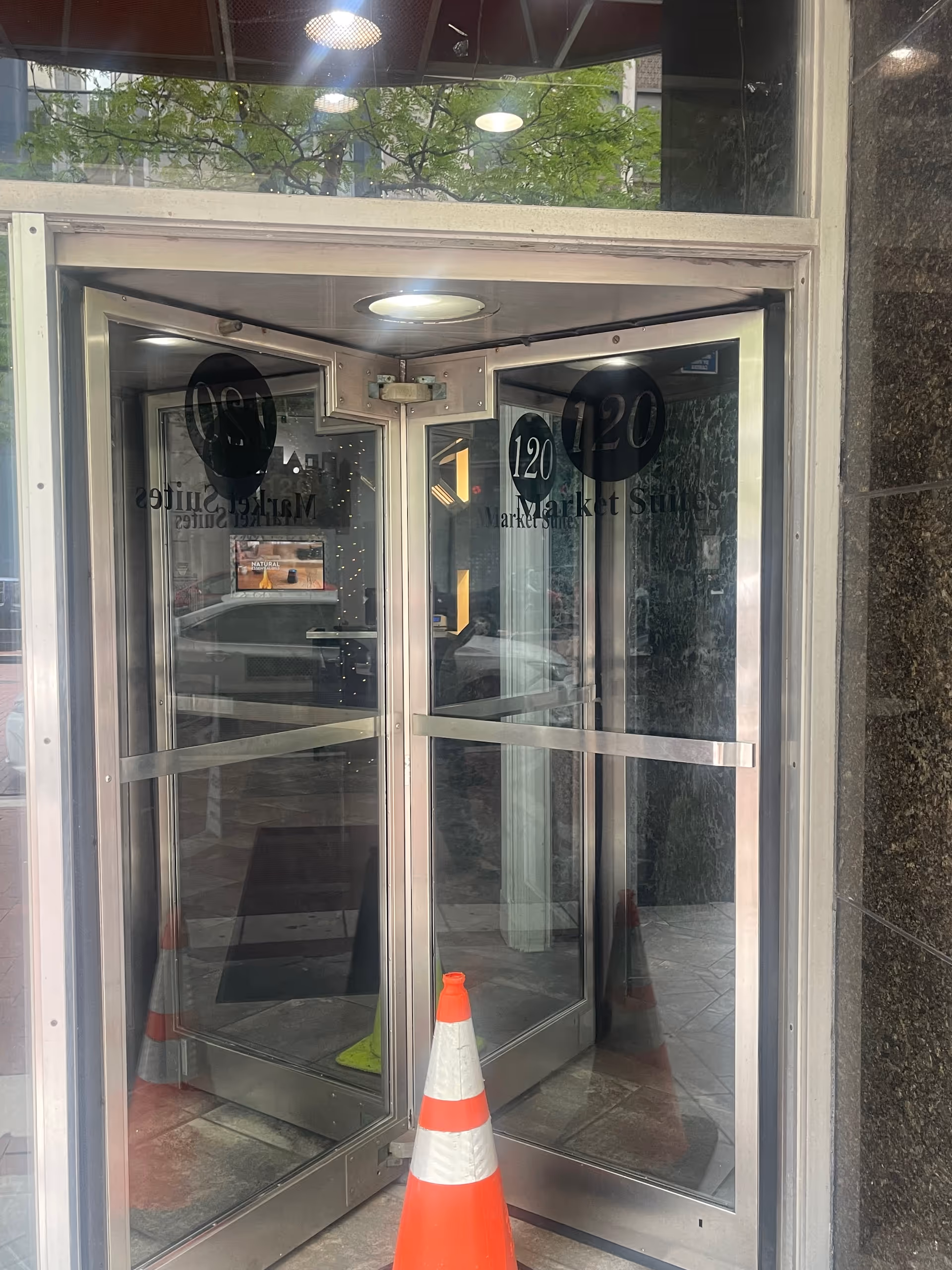 Revolving glass doors at a building entrance with a traffic cone outside.