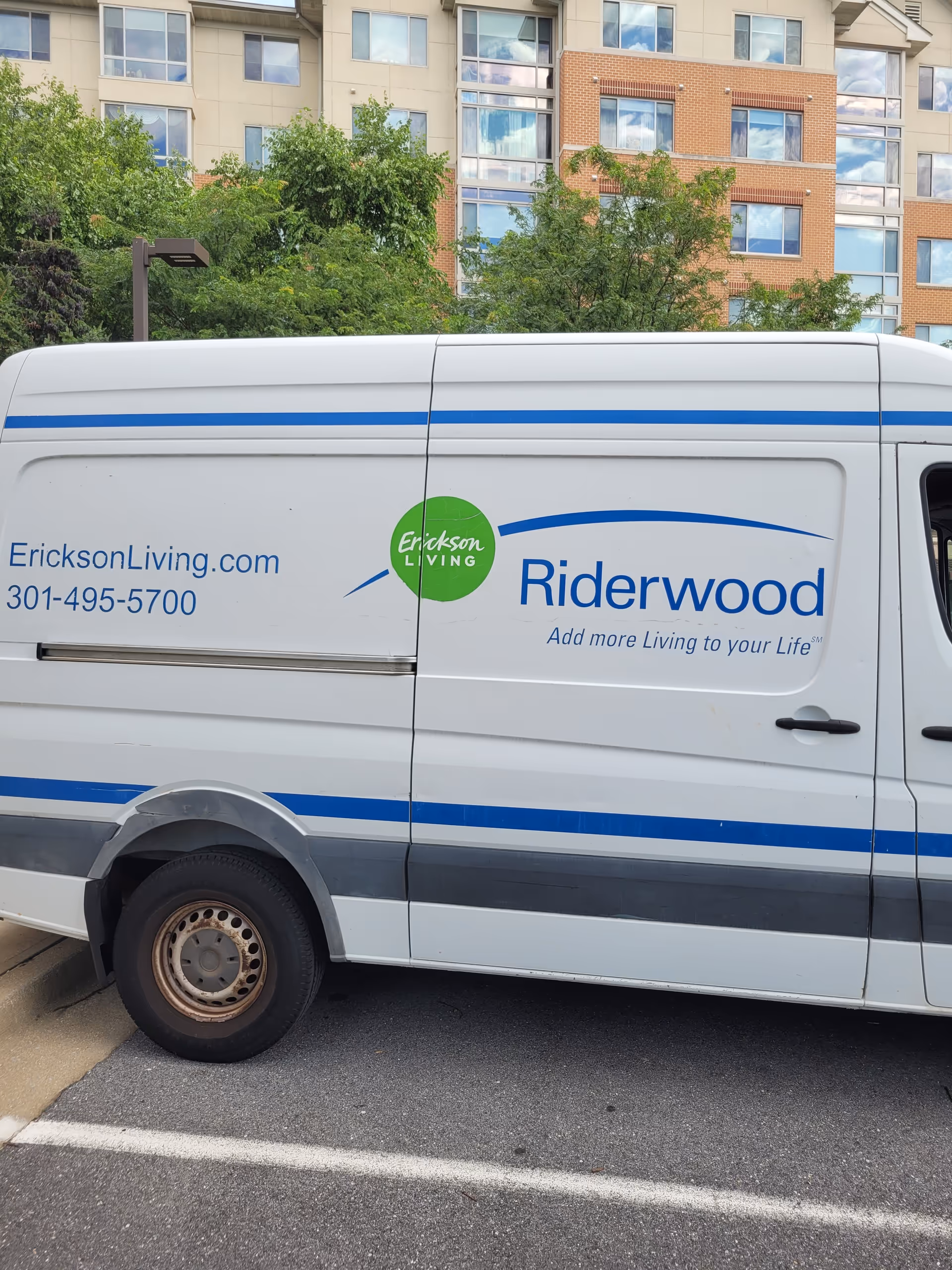 A white Erickson Living Riderwood van parked in front of a modern apartment building.