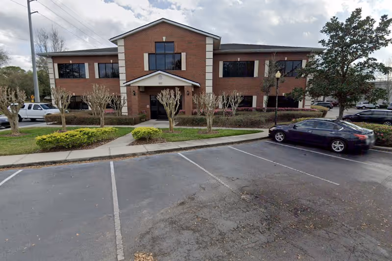 SabalCare brick senior living building with central entrance, landscaping, and nearby parked cars.