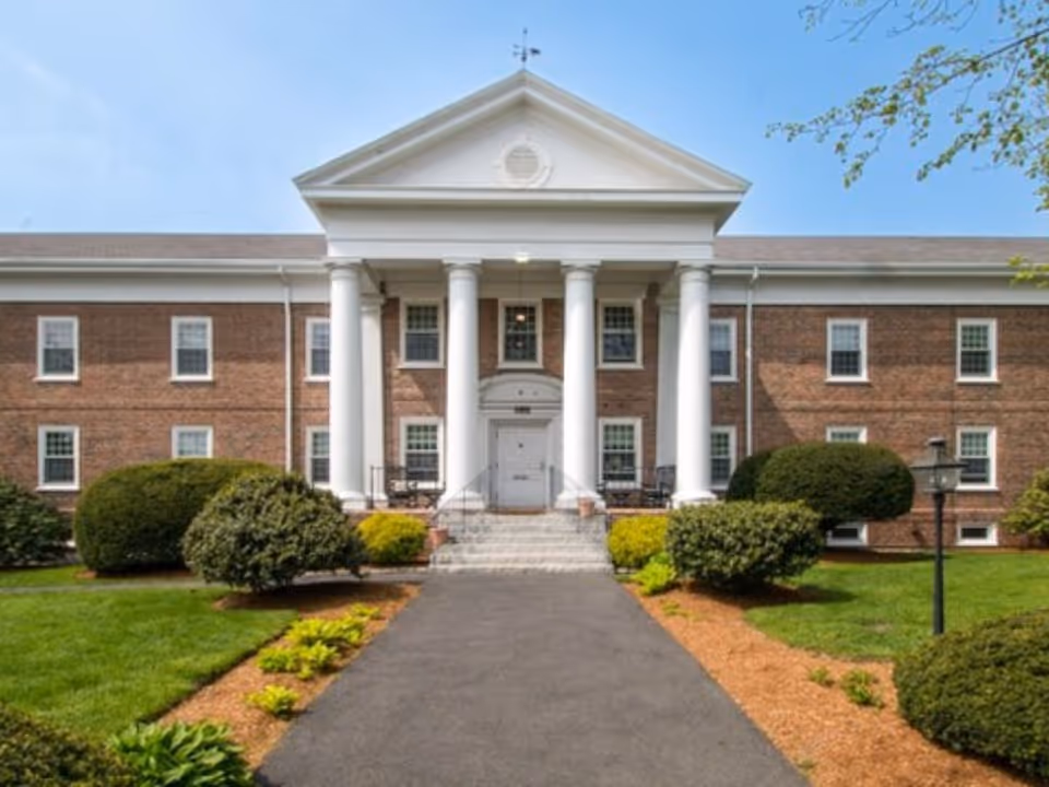 Front view of a brick elder care facility with white columns and landscaped walkway